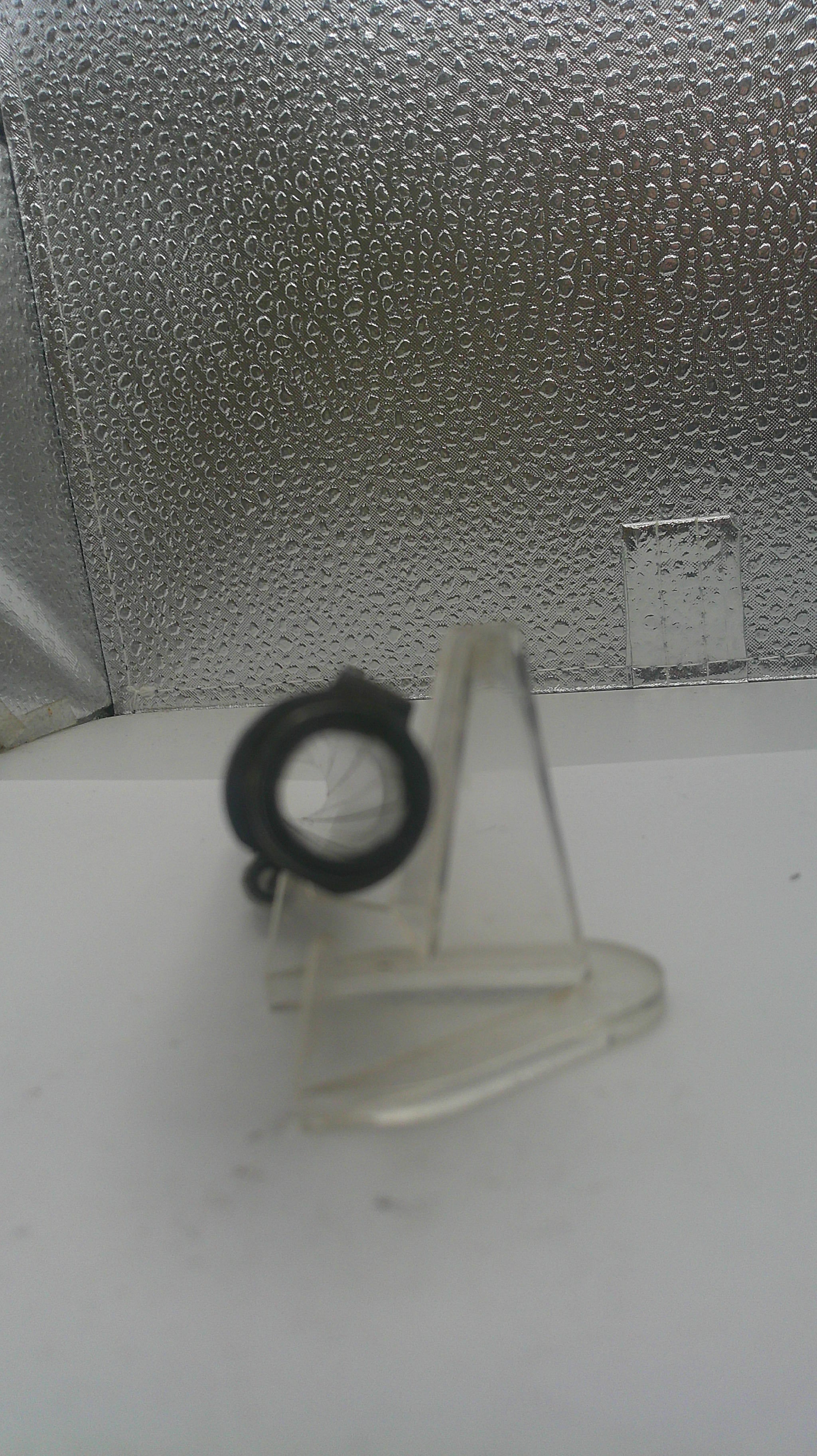 Clear plastic stand with a black ring on a textured surface