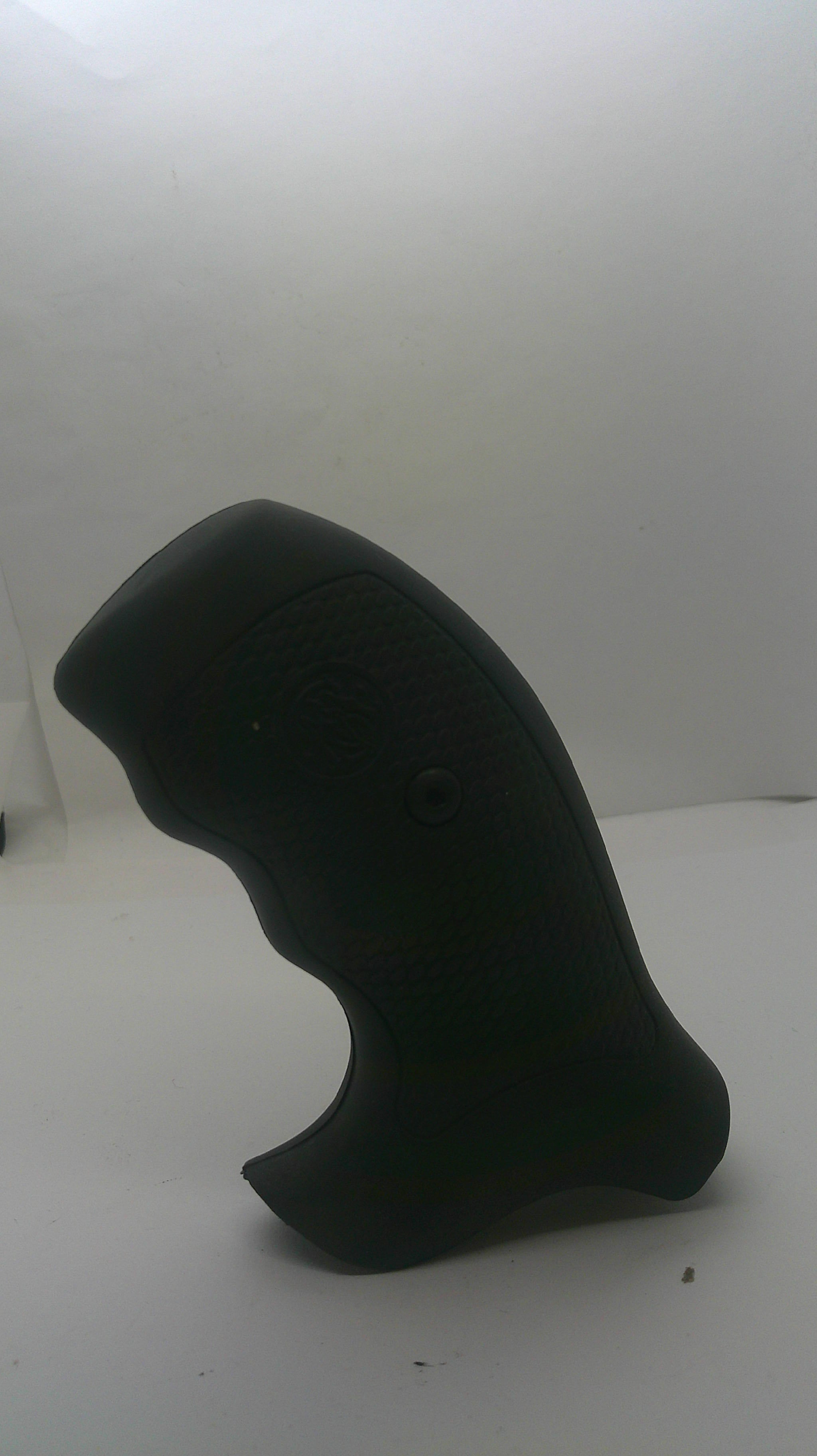 A black textured grip or handle component mounted against a plain white wall.