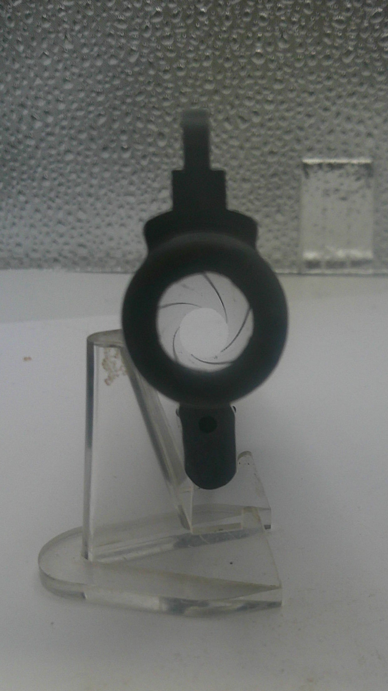Clear plastic component with black cord on a textured white surface