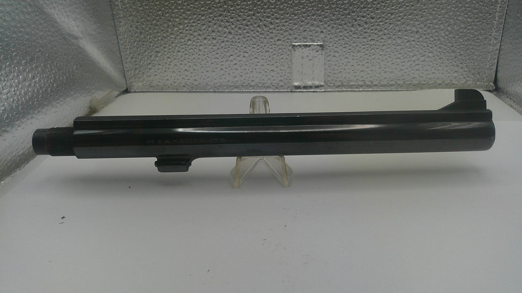 A black cylindrical gun stock or receiver component displayed horizontally on a small clear plastic stand against a textured silver backdrop.