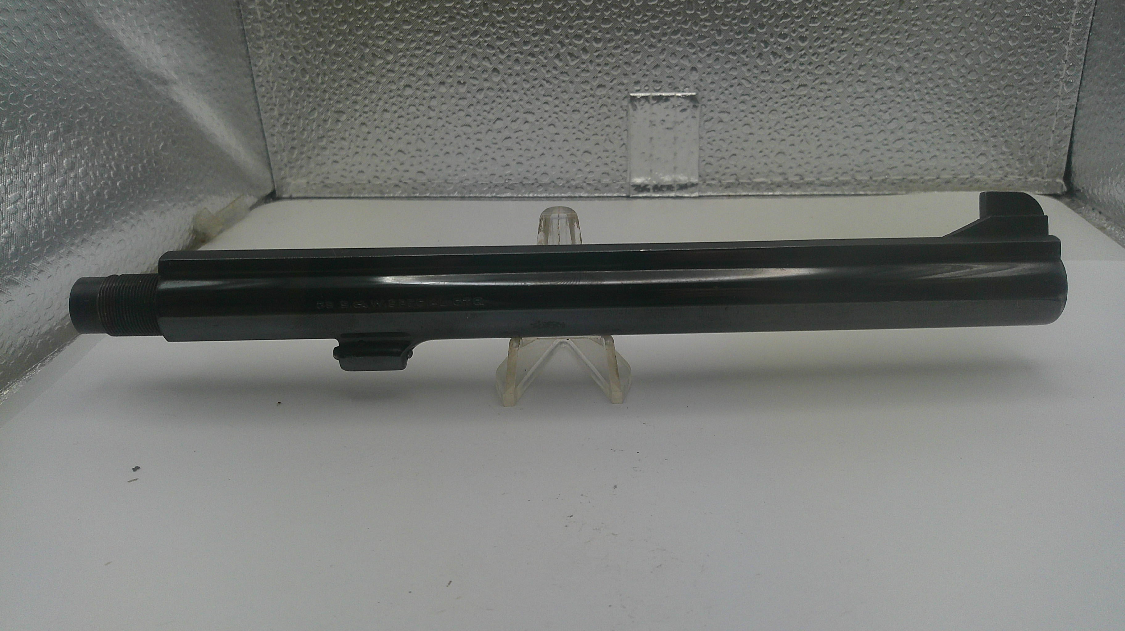 A black cylindrical gun stock or receiver component displayed horizontally on a small clear plastic stand against a textured silver backdrop.