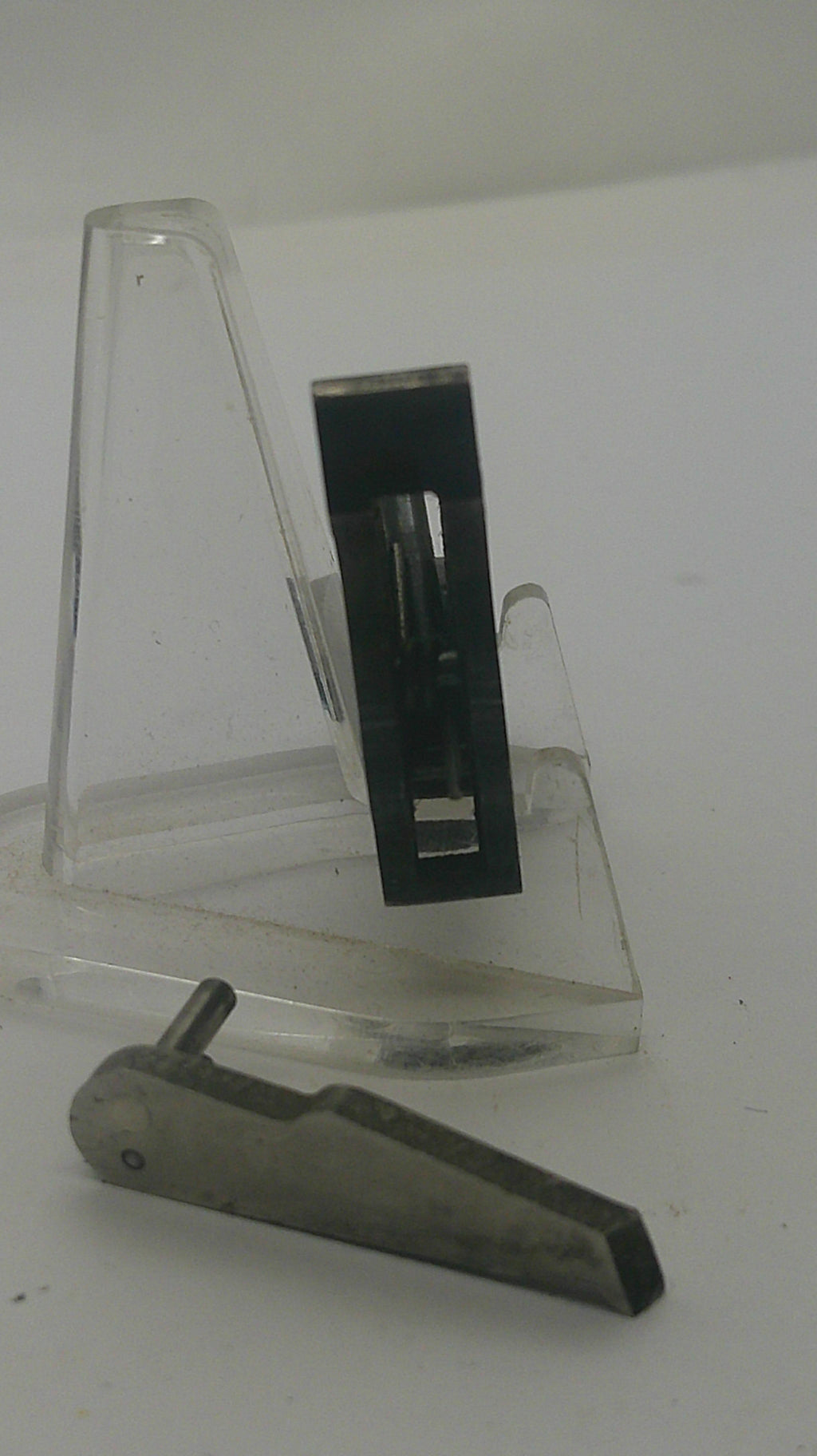 A black rectangular metal tool with a clear acrylic holder mounted on a white wall.