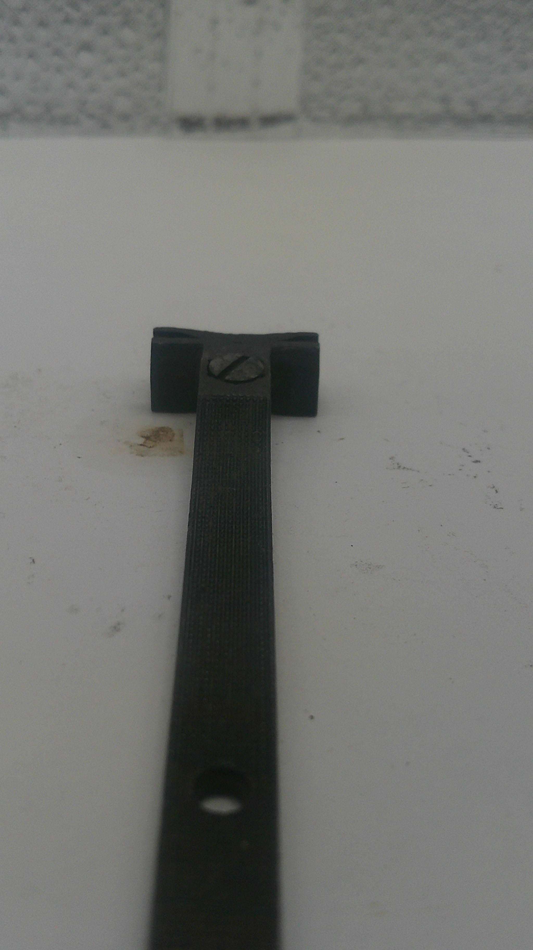 A close-up of a black metal mounting bracket or strap with a screw fastener, shown against a plain off-white background.