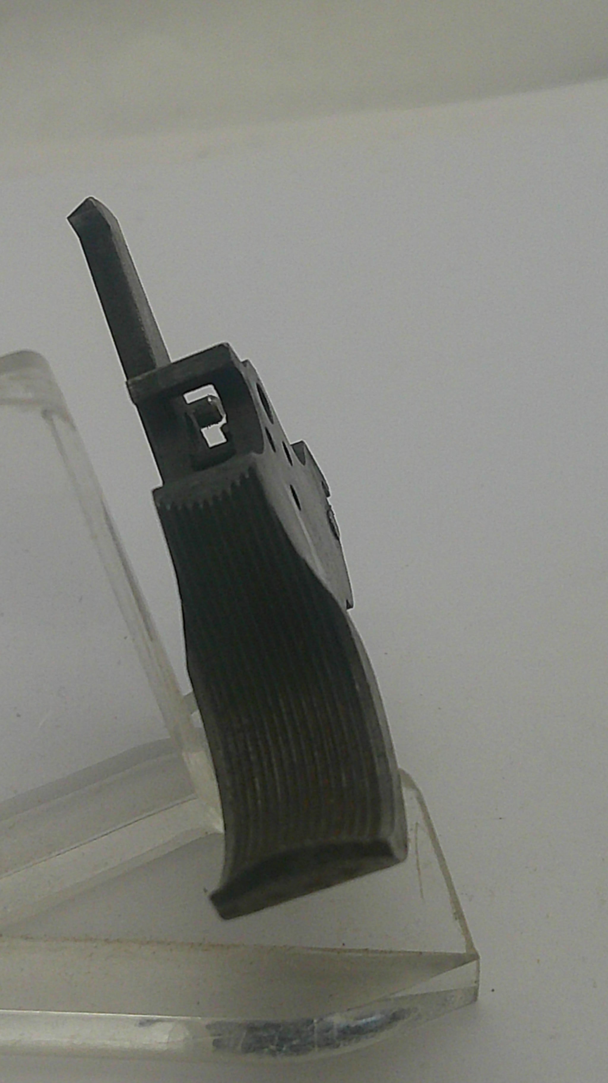 A close-up of a black textured plastic component with a small metal pin, shown against a plain light background.