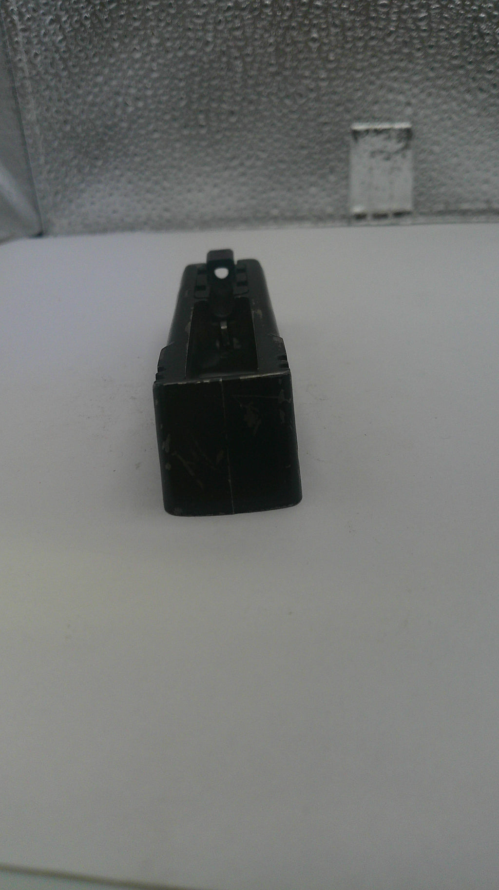 Black rectangular object on a white surface with a textured gray background