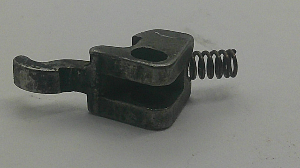 A small dark metal mechanical component with a looped spring attached, photographed on a plain light gray background.