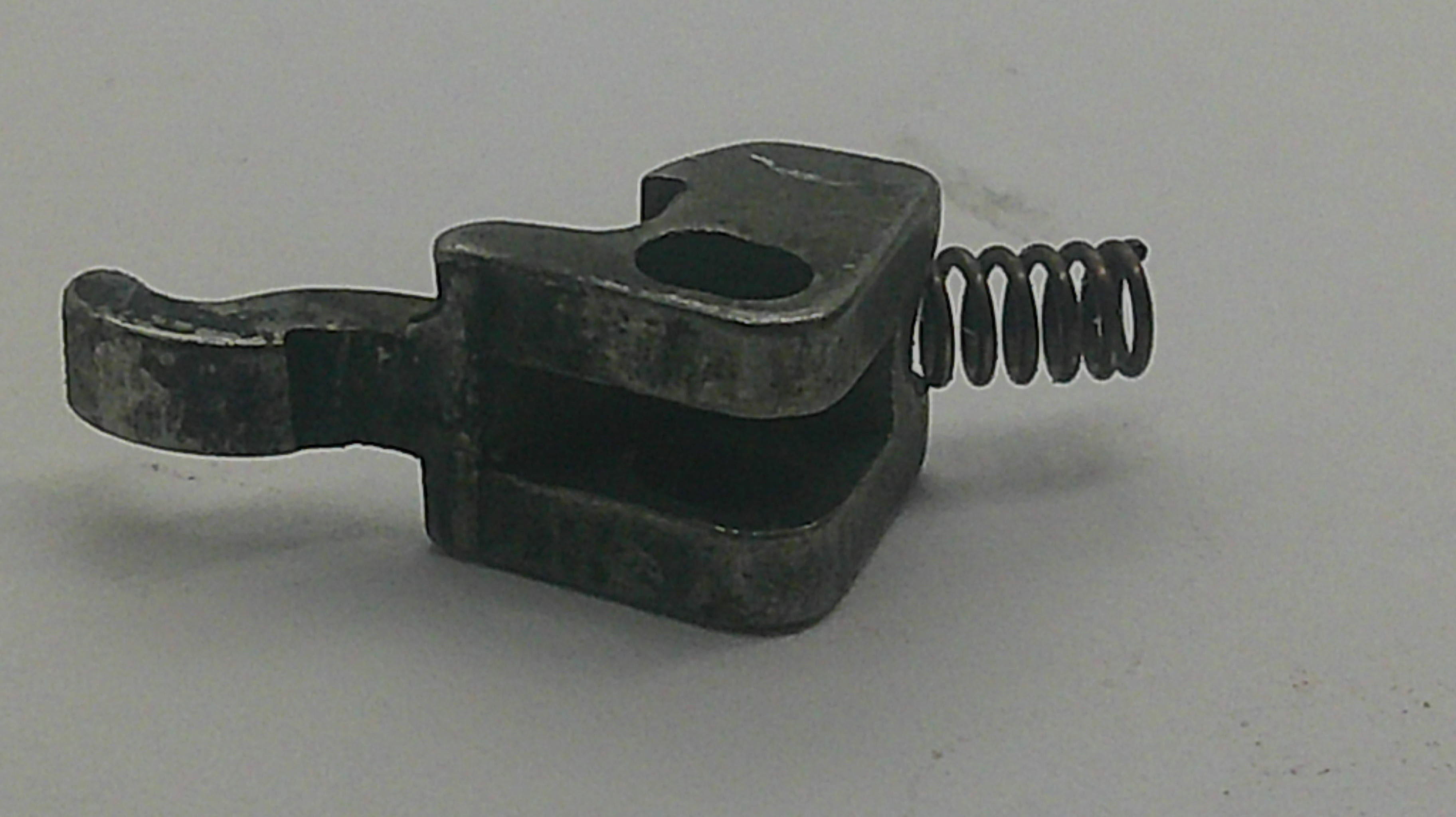 A small dark metal mechanical component with a looped spring attached, photographed on a plain light gray background.