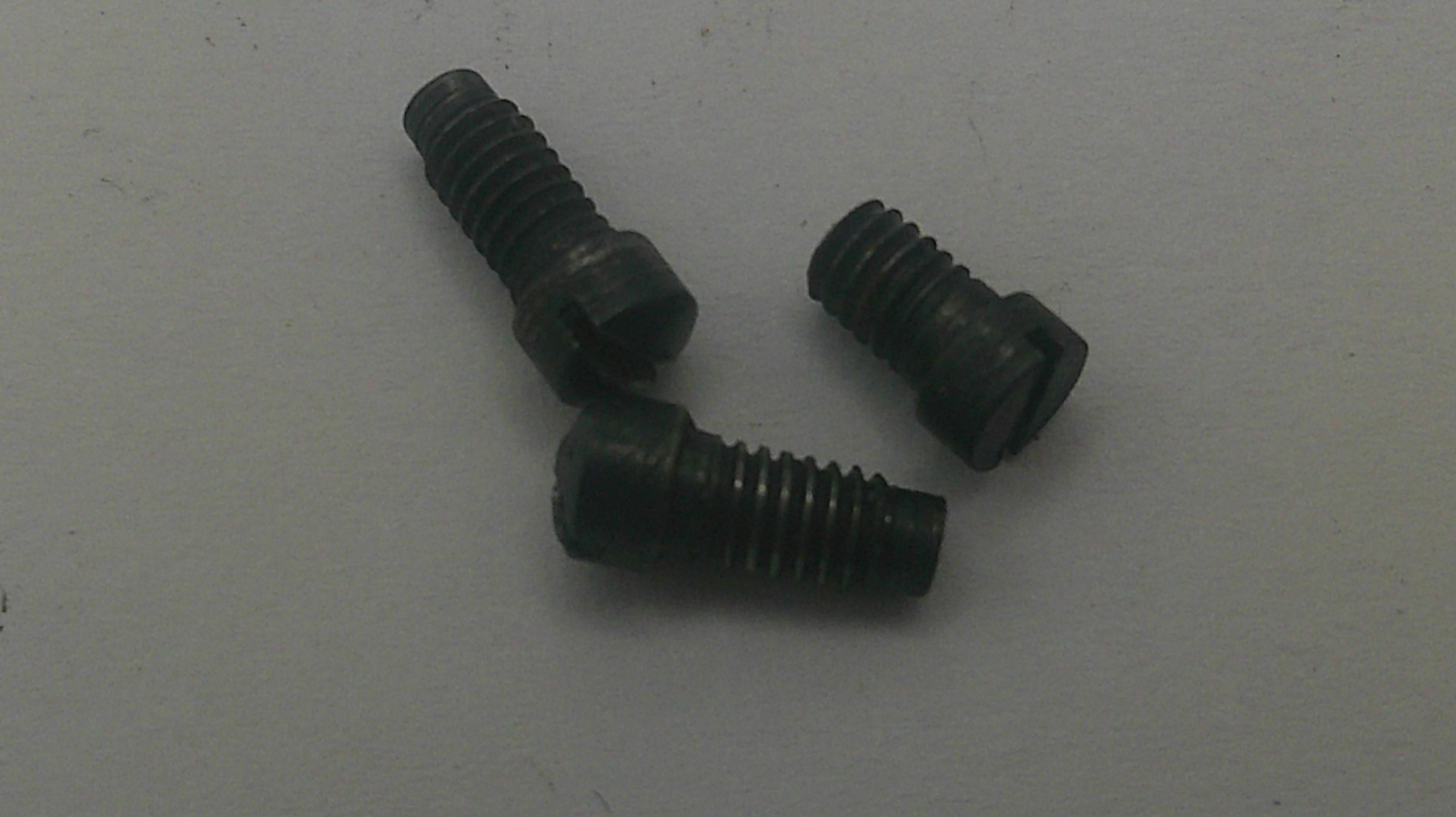 Three small black metal screws with slotted heads, arranged on a plain light gray surface.