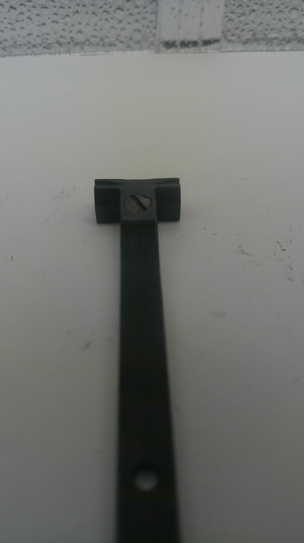 A close-up of a black metal hardware component, likely a bracket or mounting piece, attached to a white surface.