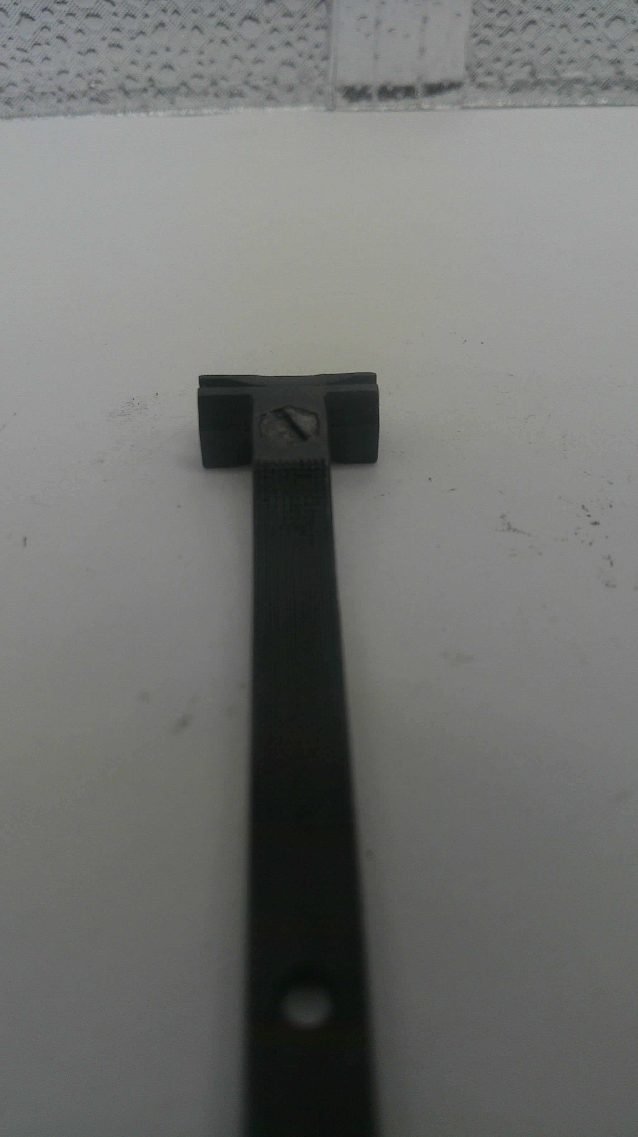 A close-up of a black metal hardware component, likely a bracket or mounting piece, attached to a white surface.