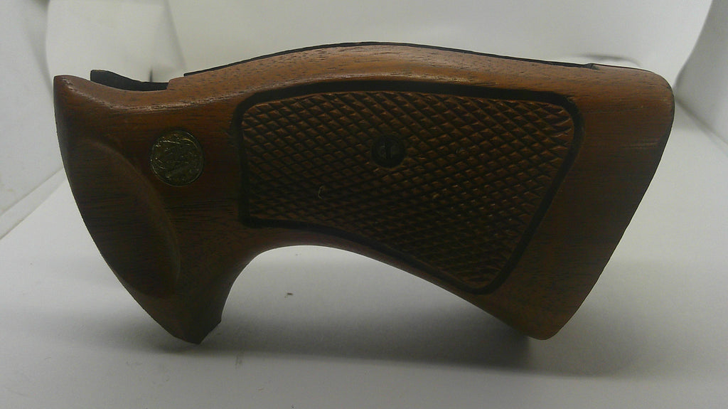 A brown wooden gun stock grip or buttstock piece with a textured checkered grip panel and a brass emblem, shown on a plain white background.