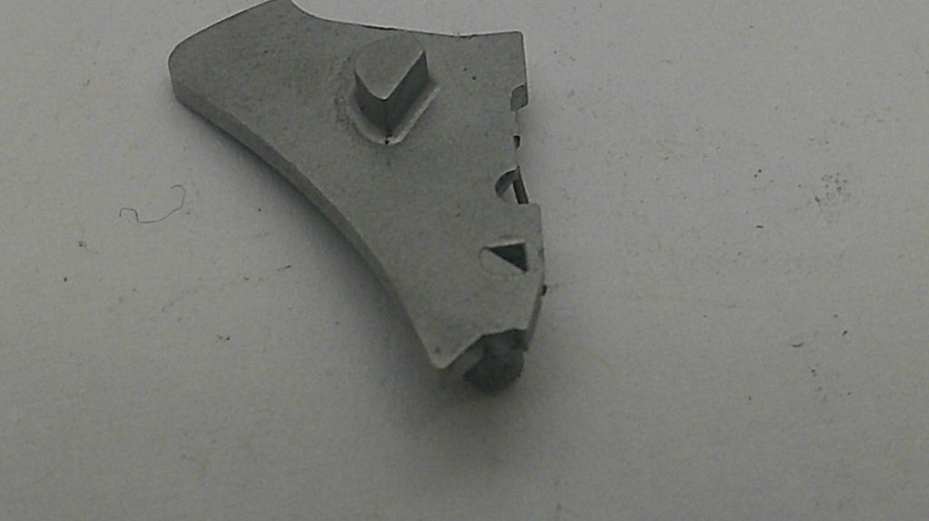 A small gray plastic or metal component with a triangular notch and cutouts, photographed on a plain light gray surface.