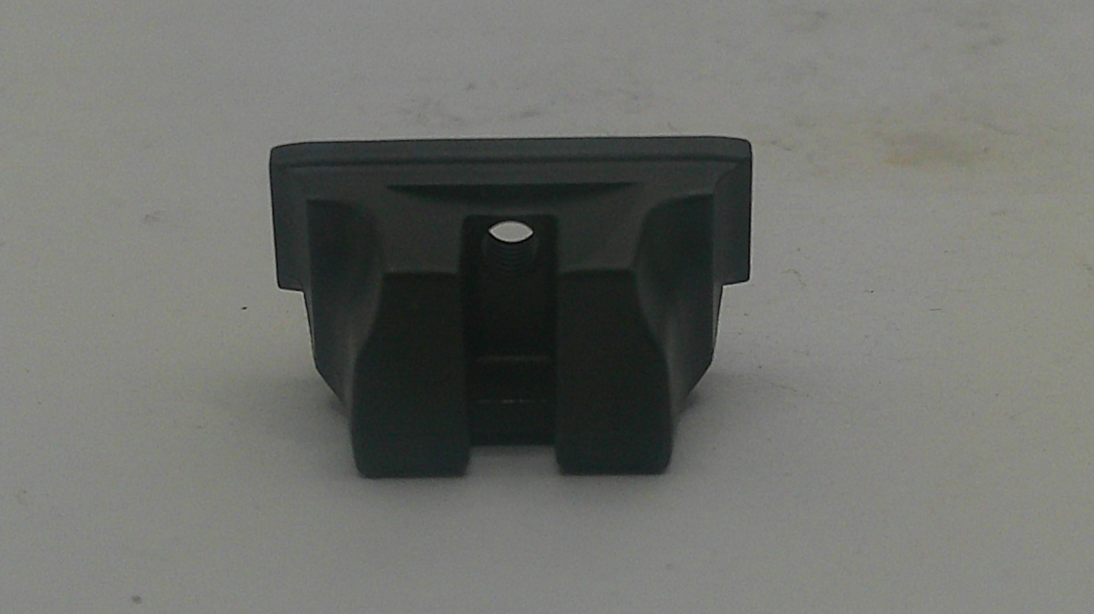 A small black plastic component or clip with a rectangular top and two angled side supports, photographed on a plain light gray surface.