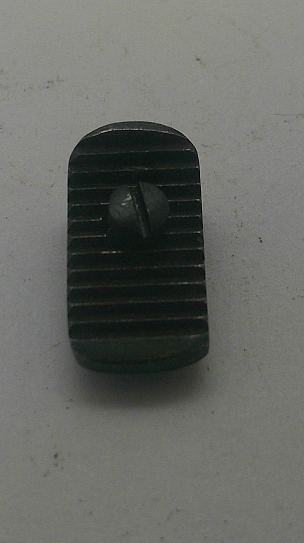 A small black plastic or metal component with a ribbed rectangular body and a central screw, photographed on a light gray surface.