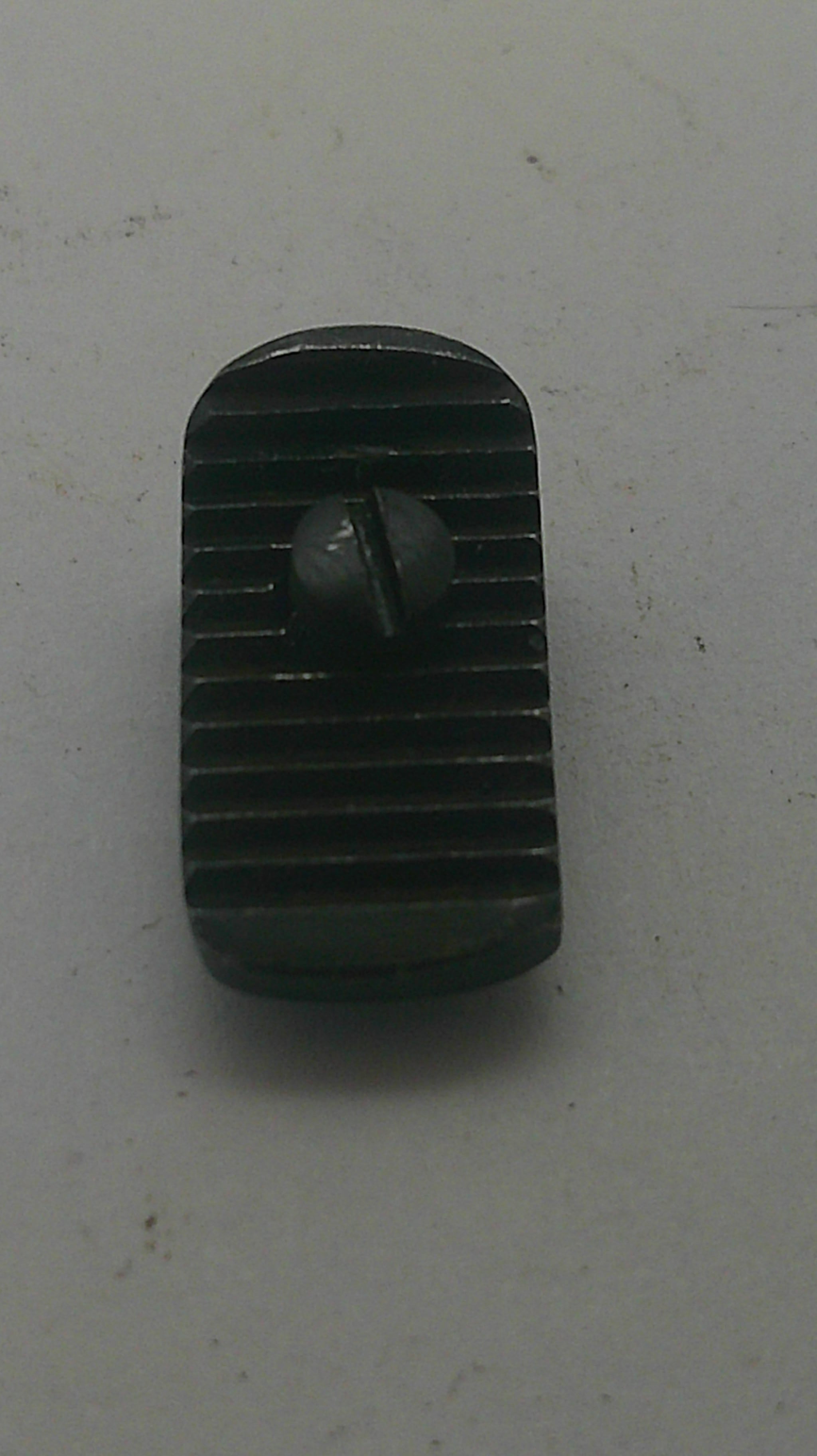 A small black plastic or metal component with a ribbed rectangular body and a central screw, photographed on a light gray surface.
