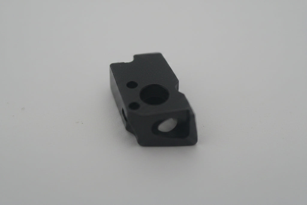 A small dark metal machined part or component photographed on a plain light background.