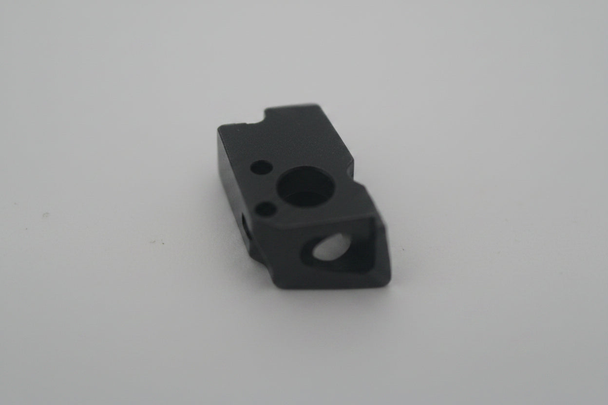 A small dark metal machined part or component photographed on a plain light background.