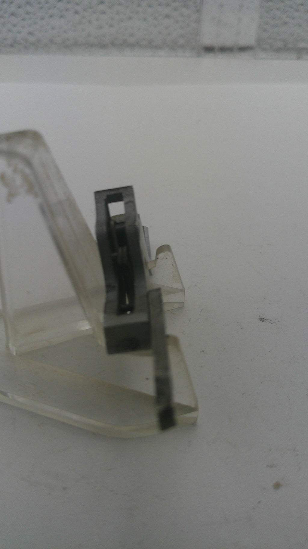Metal latch on a clear plastic strip against a white background