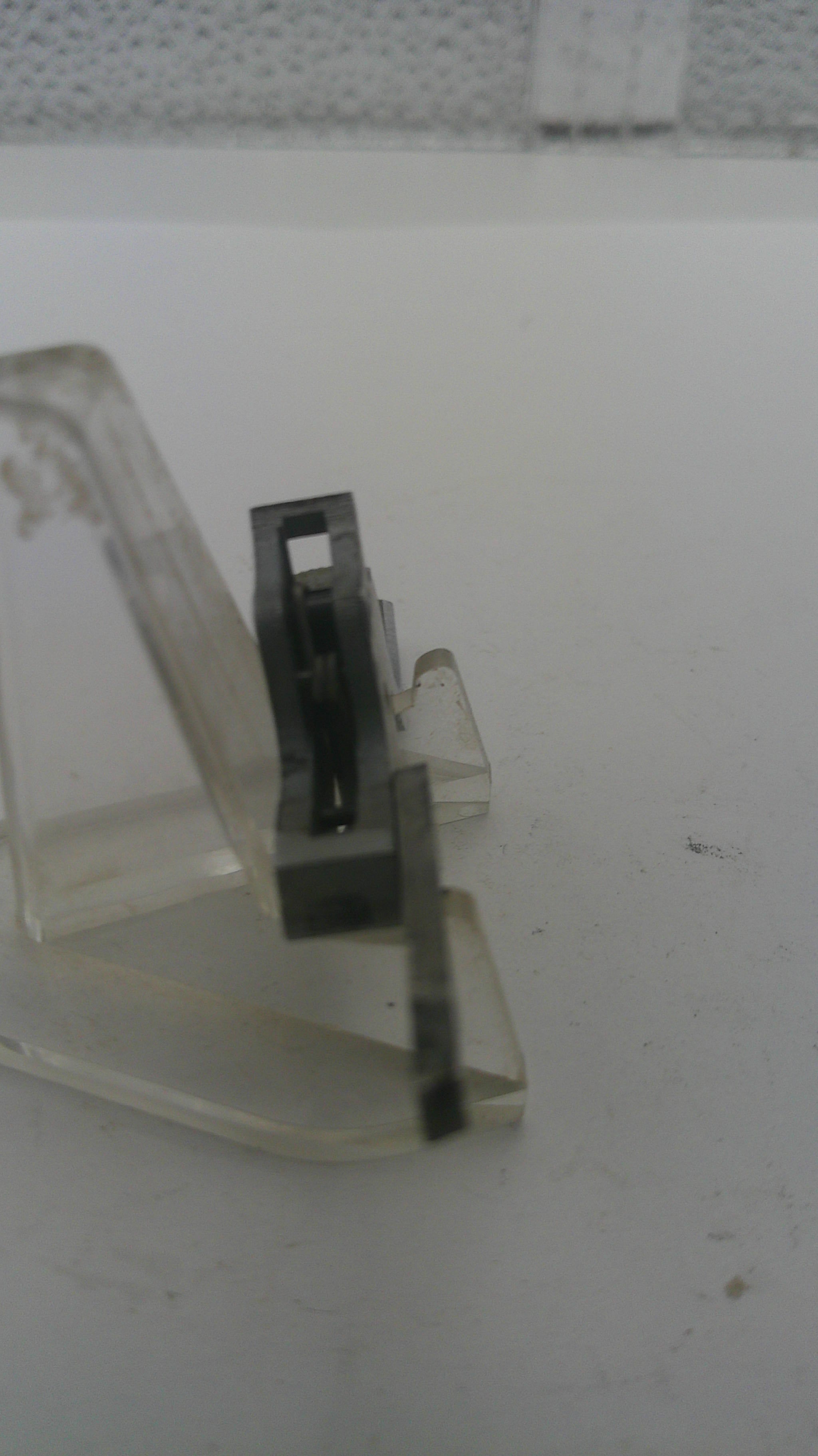 Metal latch on a clear plastic strip against a white background