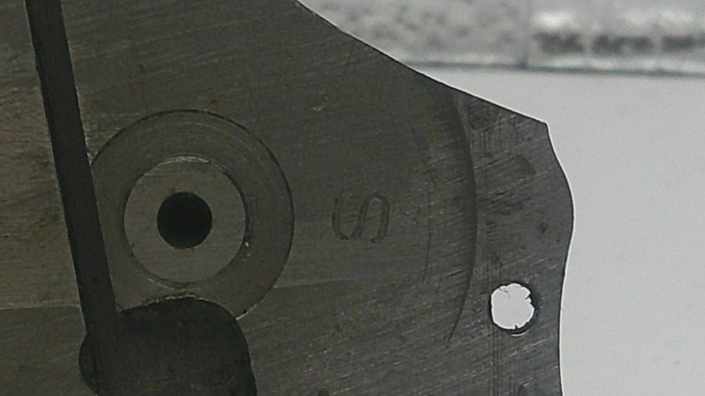 Close-up of a metal tool with a circular hole and 'S' marking on a blurred background