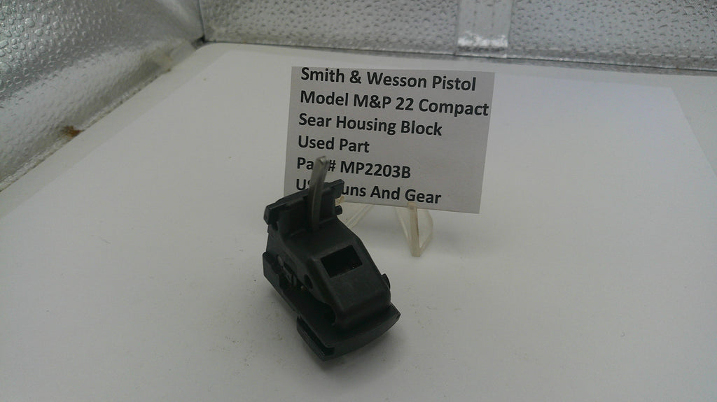 Black firearm part on a white surface with a label indicating brand and model details.