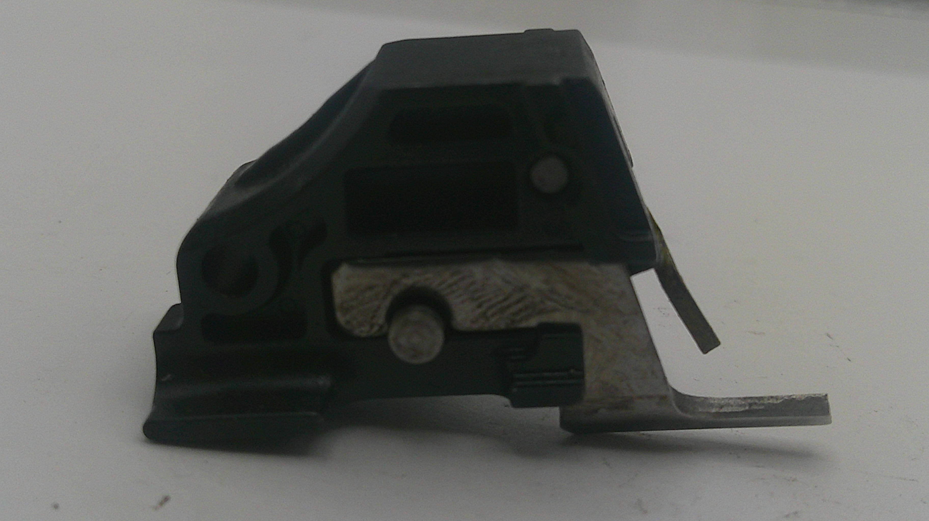 A small black plastic and silver metal mechanical component, likely a latch or switch part, photographed on a plain light gray surface.