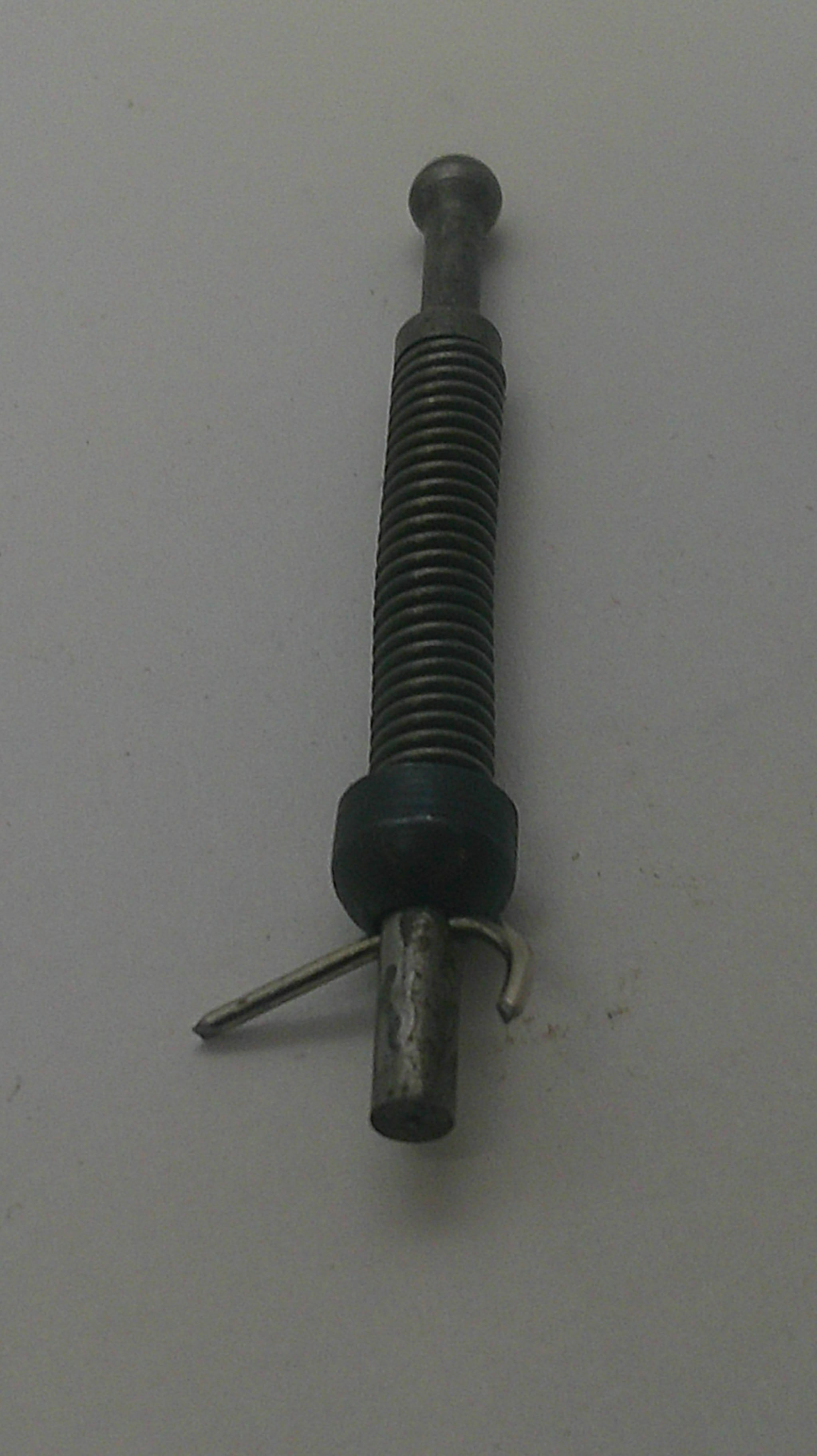 A small metal mechanical component with a threaded rod, a dark green plastic or rubber ring, and a bent metal pin, photographed on a plain light gray surface.