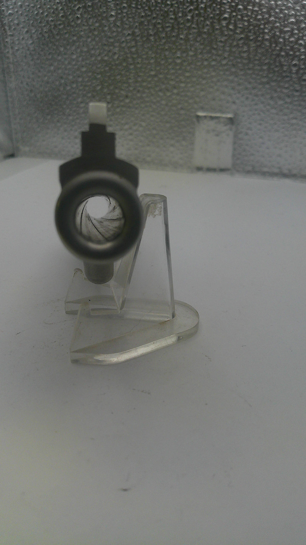 Clear plastic stand with a black circular object on a textured surface