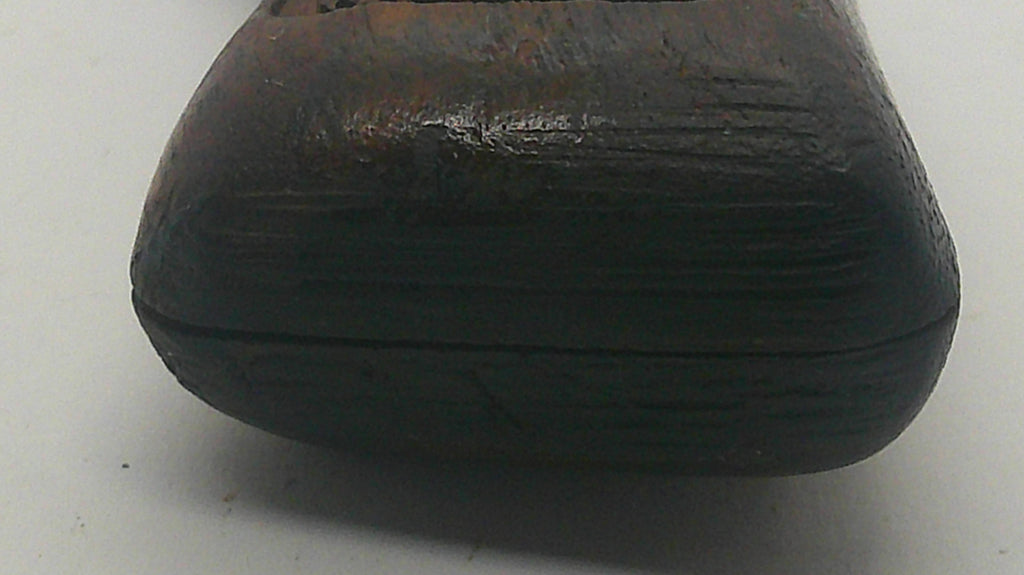A close-up of a dark brown carved wooden object, showing a textured grain and a circular cutout at the top, set against a plain light gray background.
