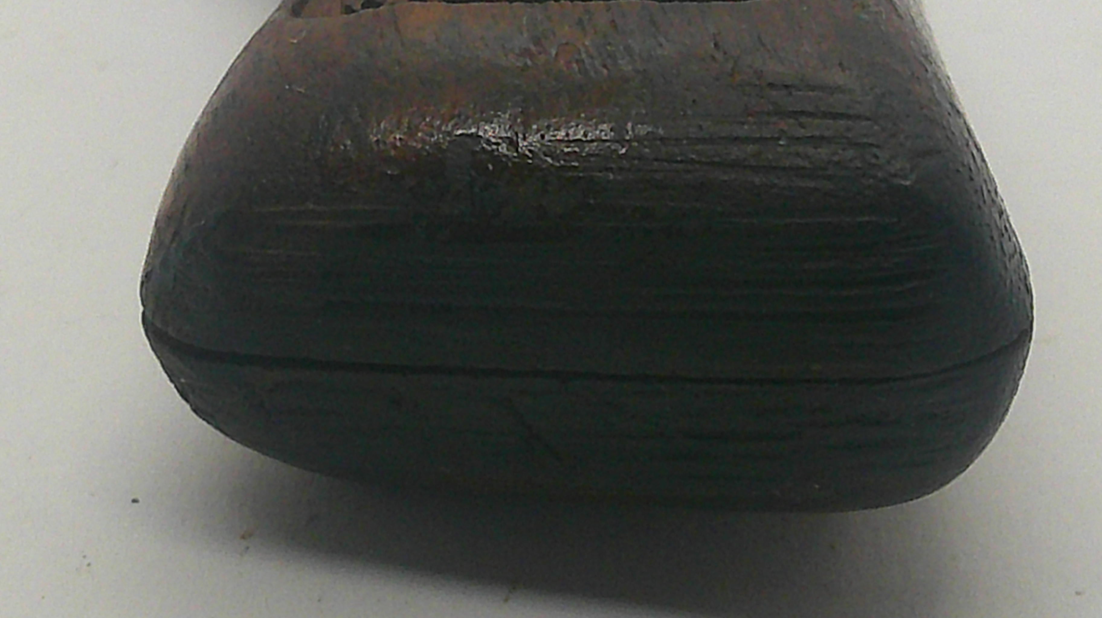 A close-up of a dark brown carved wooden object, showing a textured grain and a circular cutout at the top, set against a plain light gray background.
