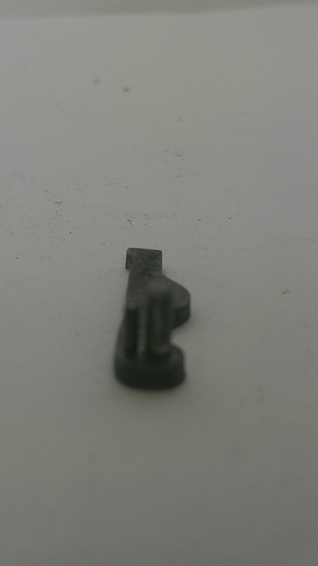 A small dark gray plastic hook or clip mounted on a plain off-white surface.