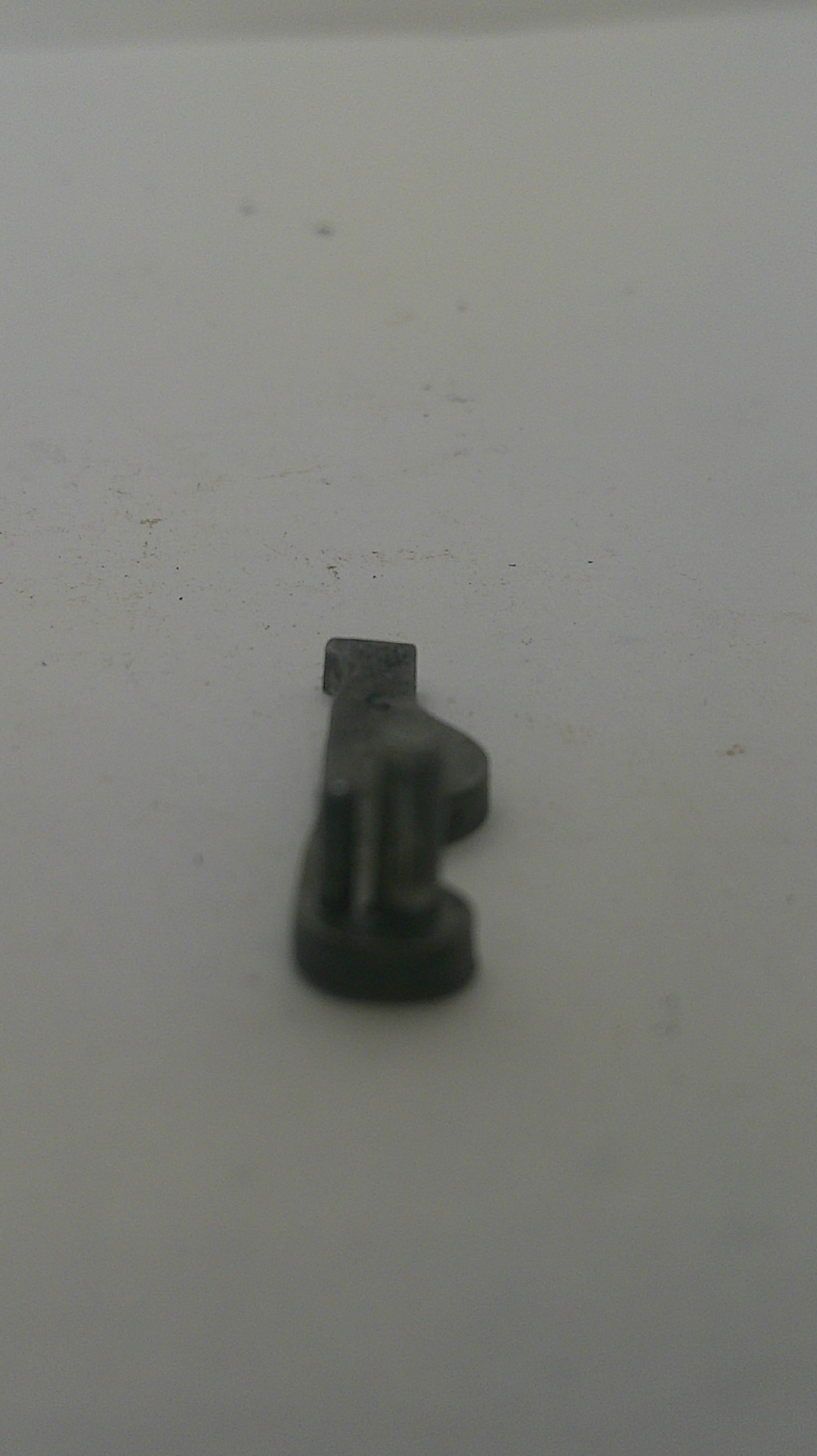 A small dark gray plastic hook or clip mounted on a plain off-white surface.