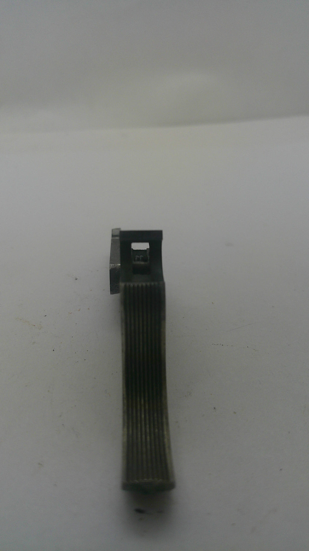 A small dark gray metal mechanical component or clip with a ribbed cylindrical body and a flat rectangular end, shown on a plain off-white background.
