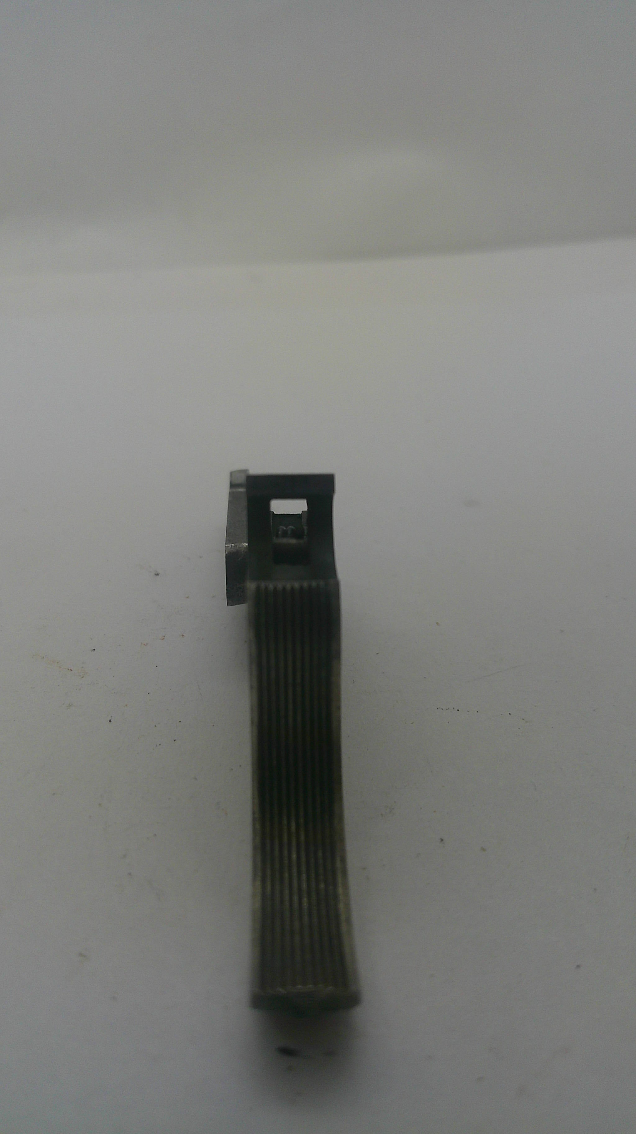 A small dark gray metal mechanical component or clip with a ribbed cylindrical body and a flat rectangular end, shown on a plain off-white background.