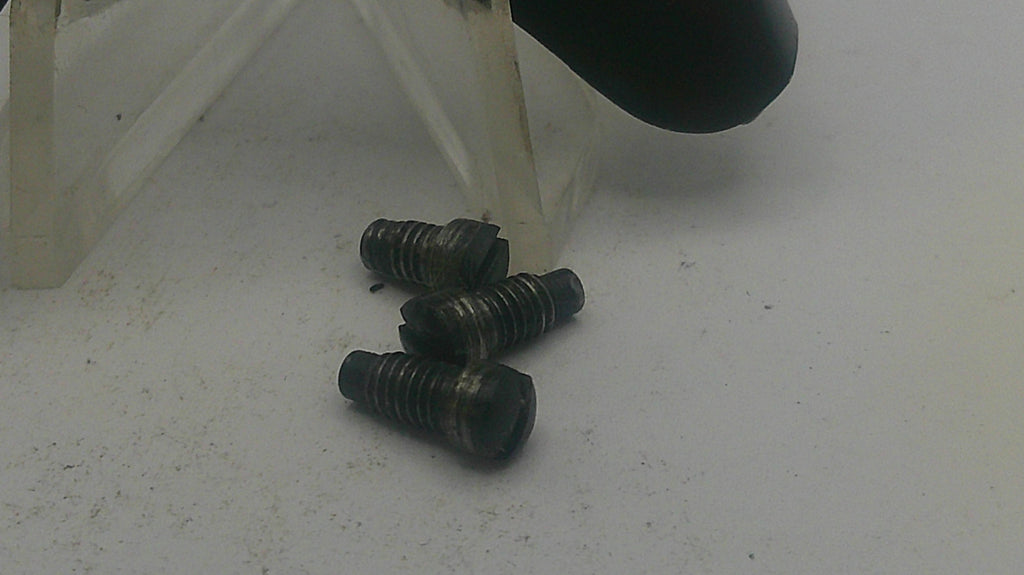 Three black screws on a white surface with a clear plastic object in the background.