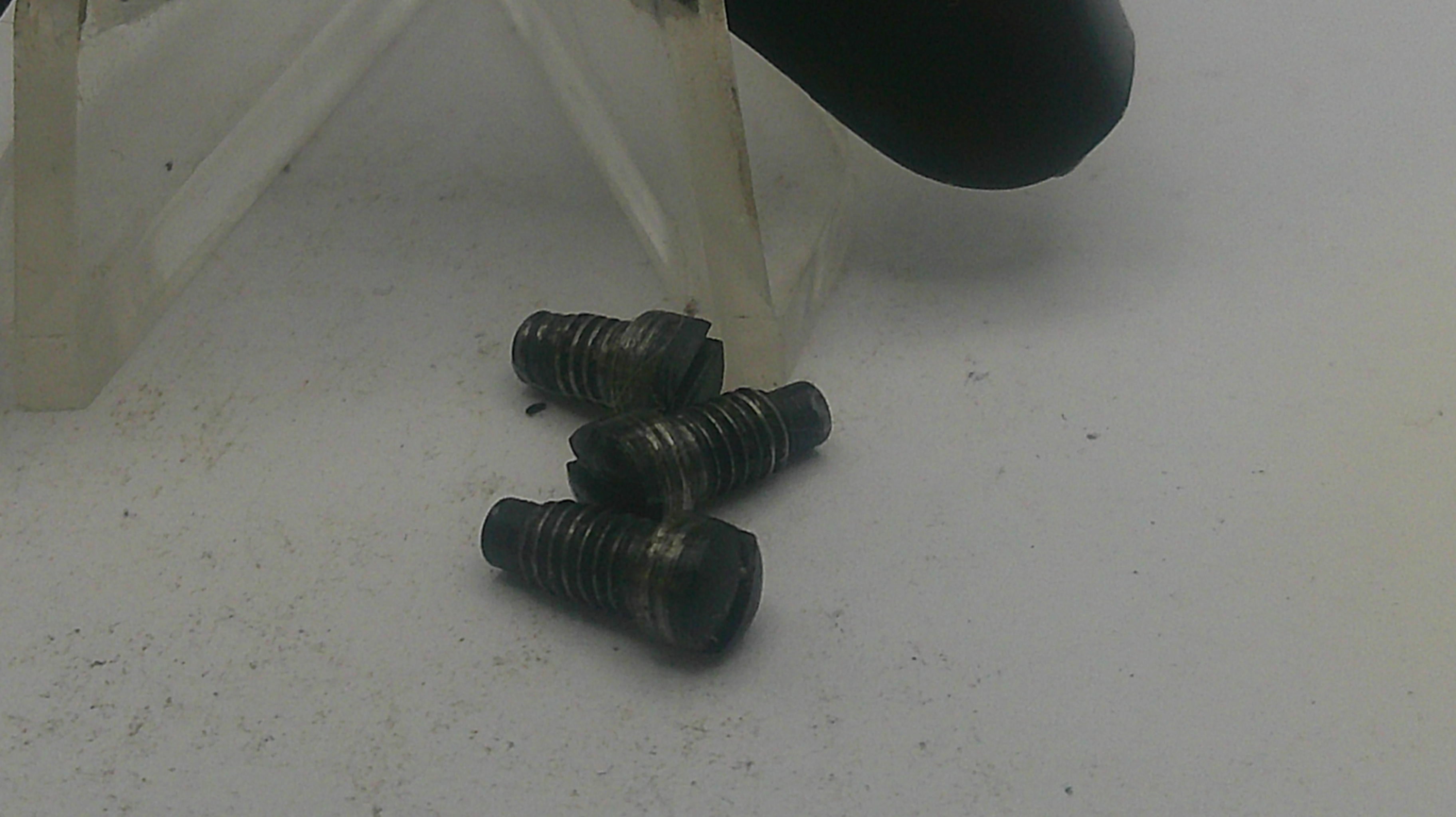 Three black screws on a white surface with a clear plastic object in the background.