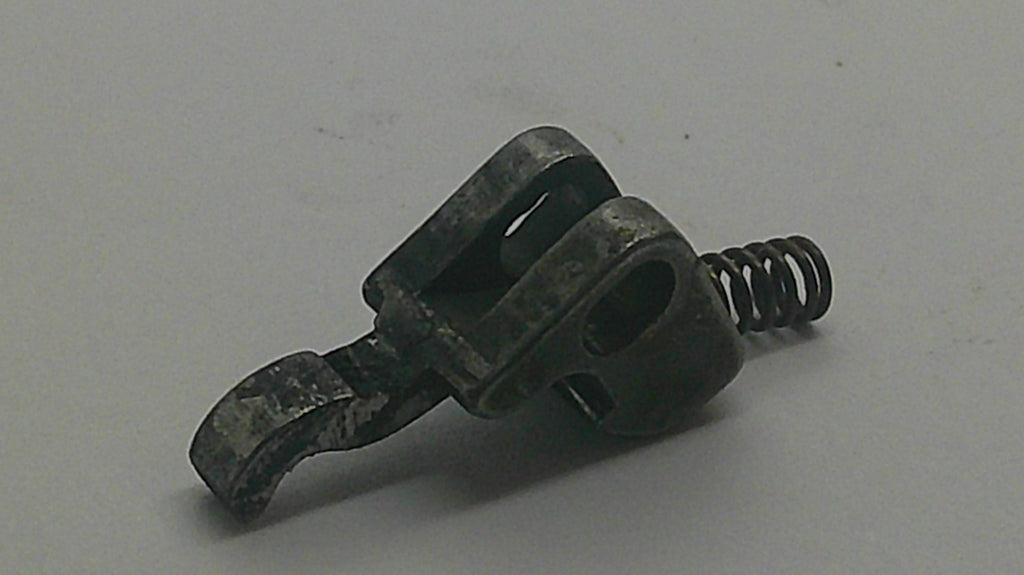 A small dark metal hardware component with a hook-like arm and a coiled spring, photographed on a plain light gray background.