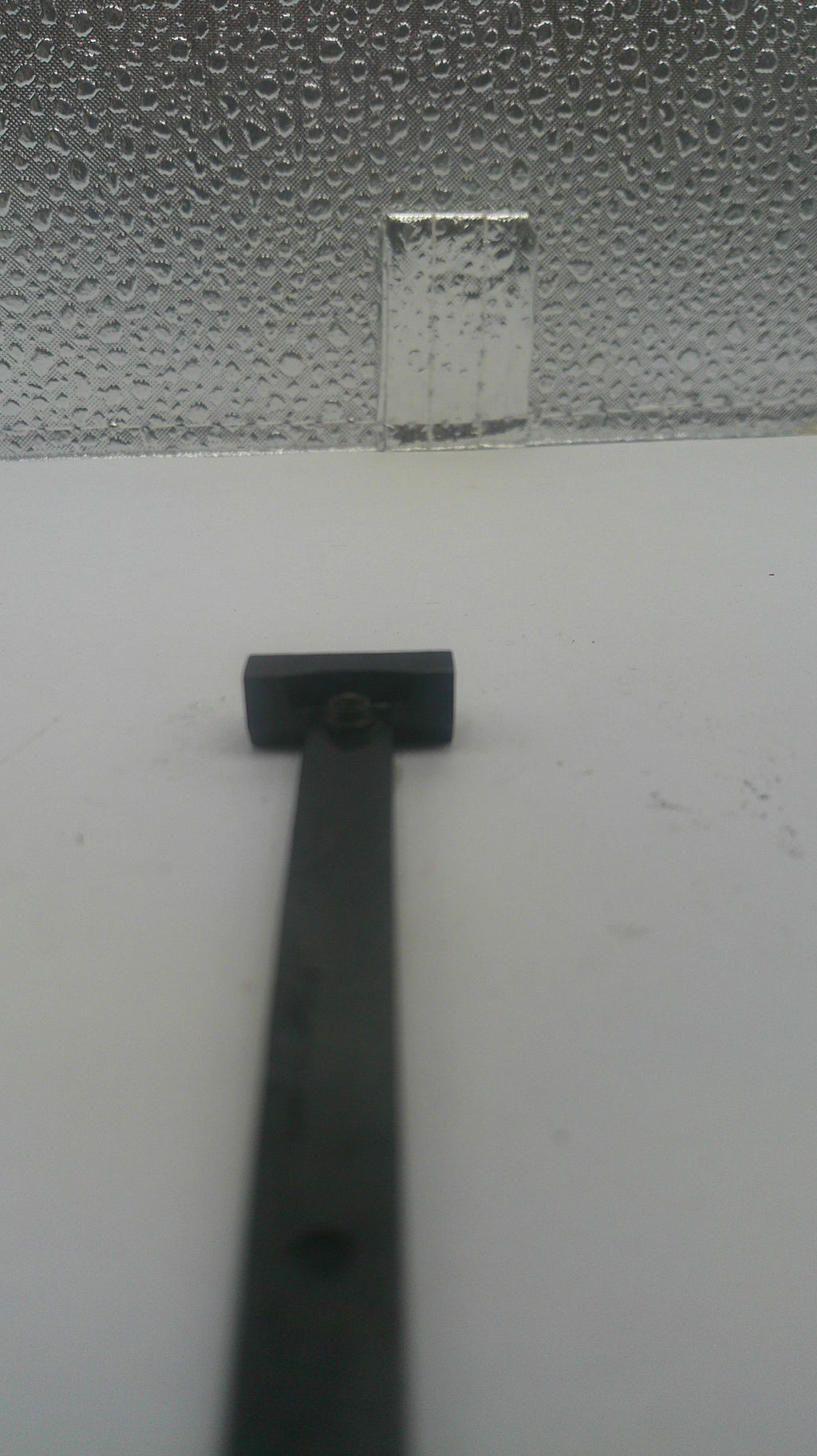 A close-up of a black metal door hinge mounted on a white door next to a textured glass panel covered in condensation.