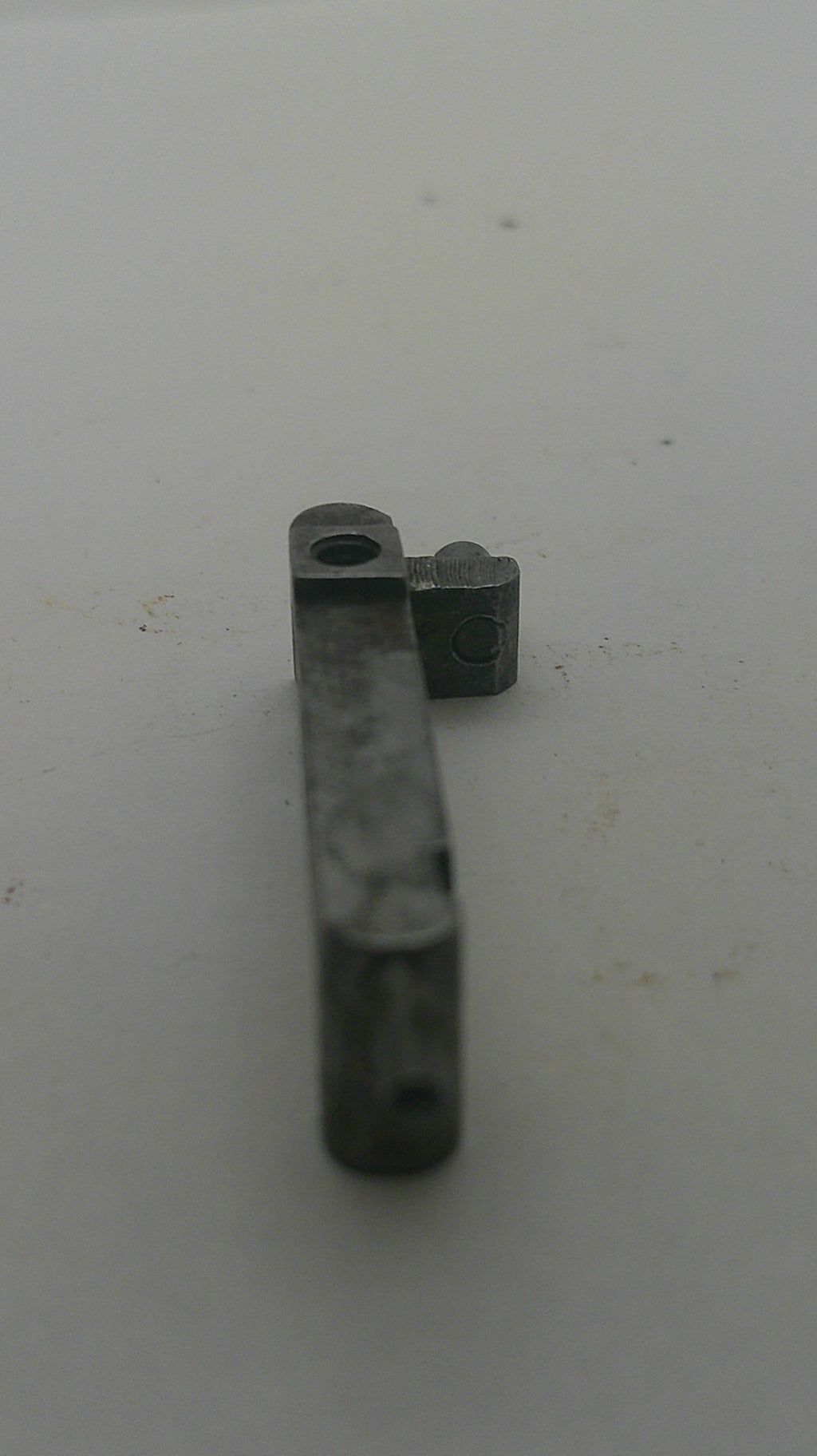A small dark gray metal hardware component, possibly a bracket or latch piece, shown against a plain off-white background.