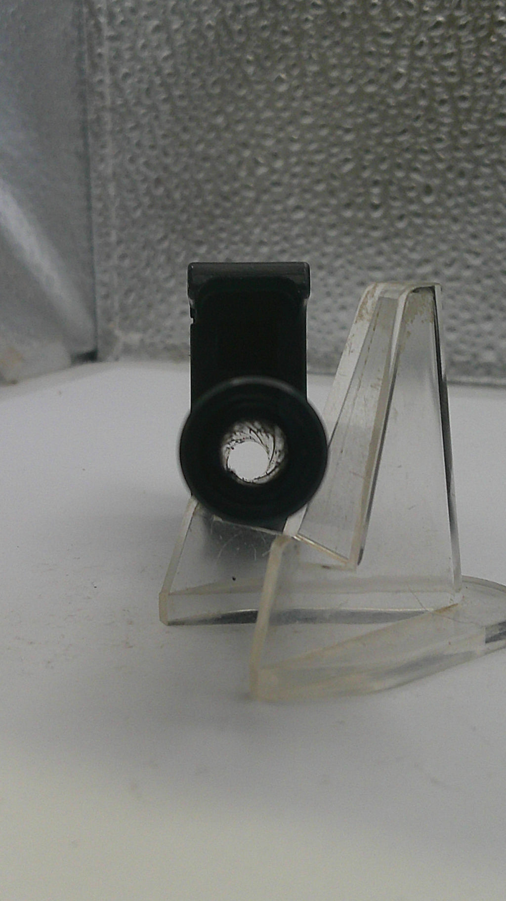 Close-up of a metal bracket with a clear plastic cover on a textured surface.