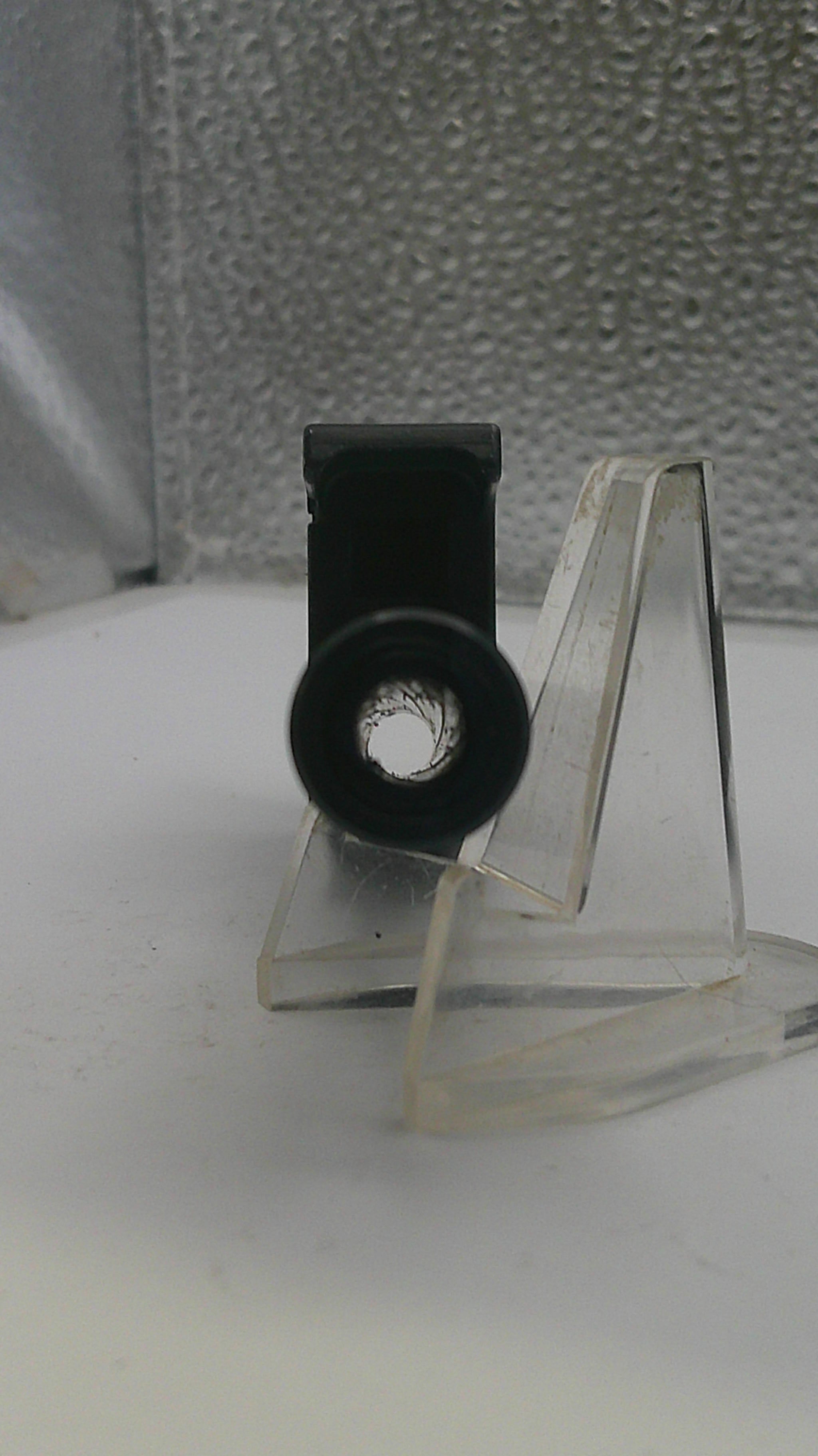 Close-up of a metal bracket with a clear plastic cover on a textured surface.