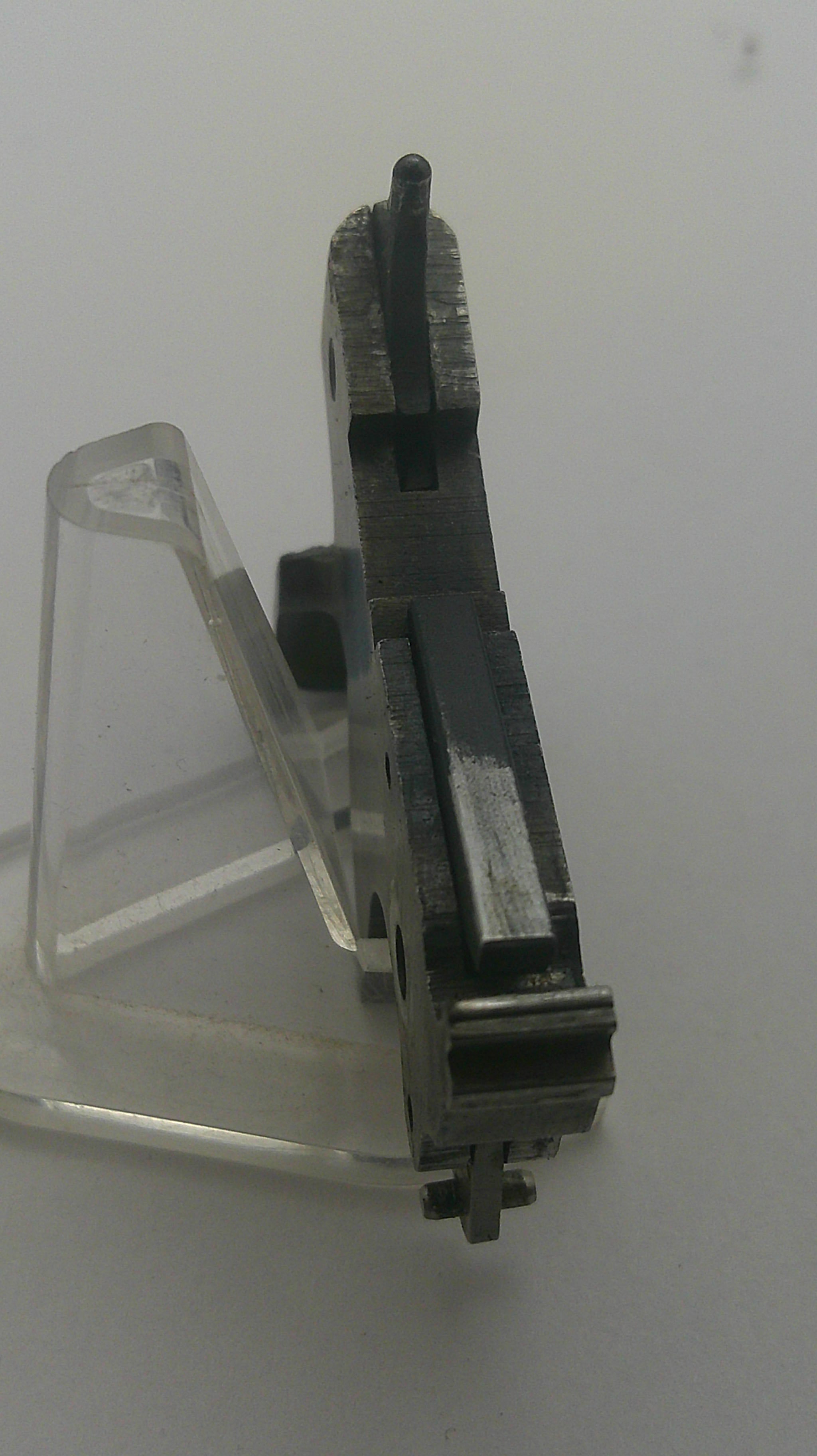 A close-up of a dark metal mechanical component or tool part with a clear plastic cover, photographed against a plain light background.