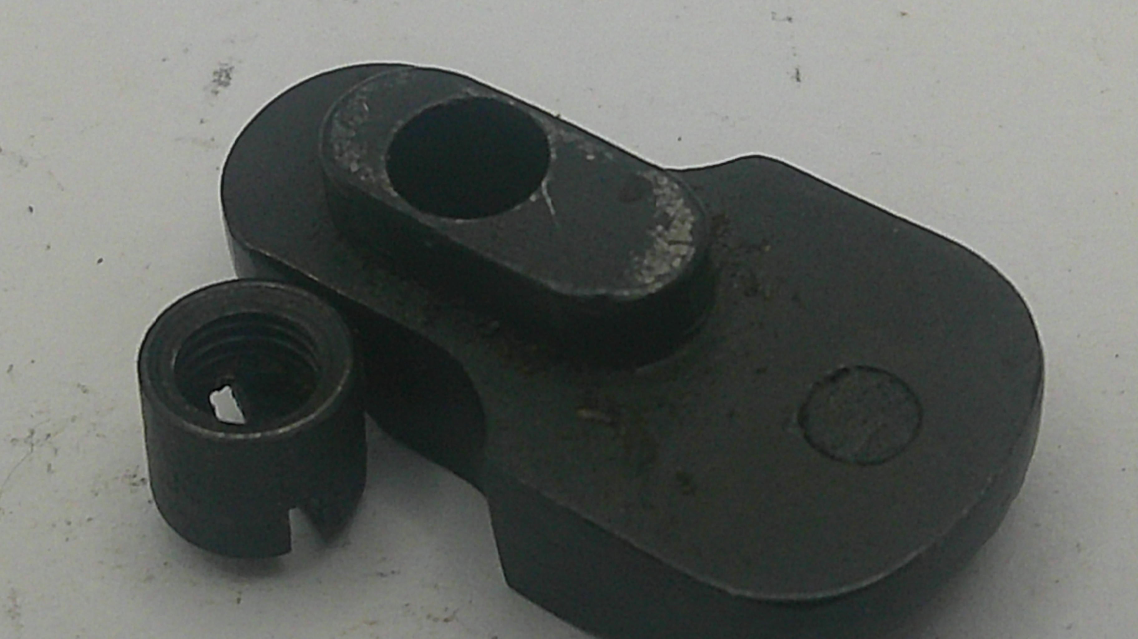 A black metal mechanical component with a threaded hole, photographed on a light gray surface.
