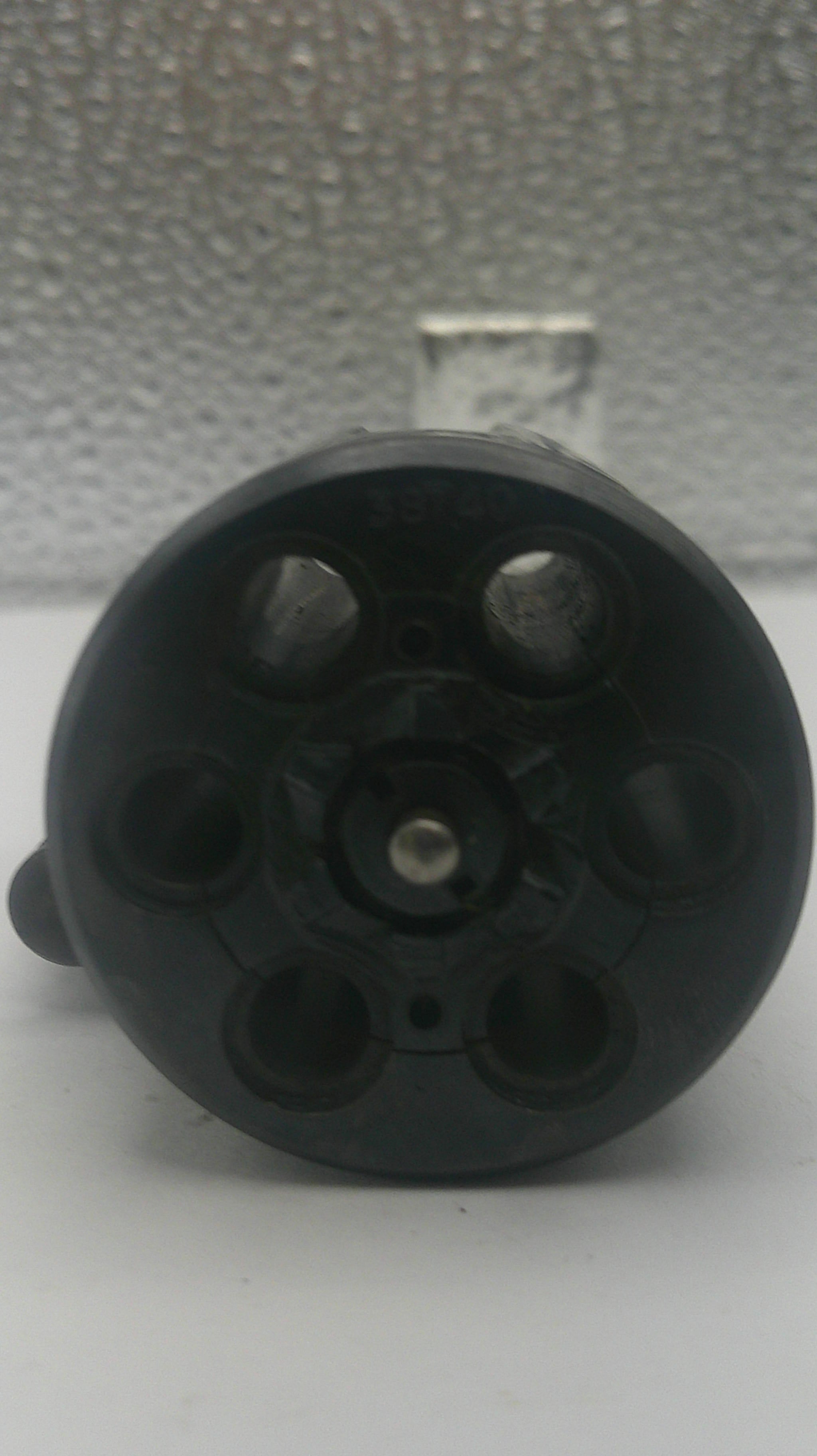 A close-up of a black plastic six-hole revolver magazine or gun holster component, photographed against a textured gray background.