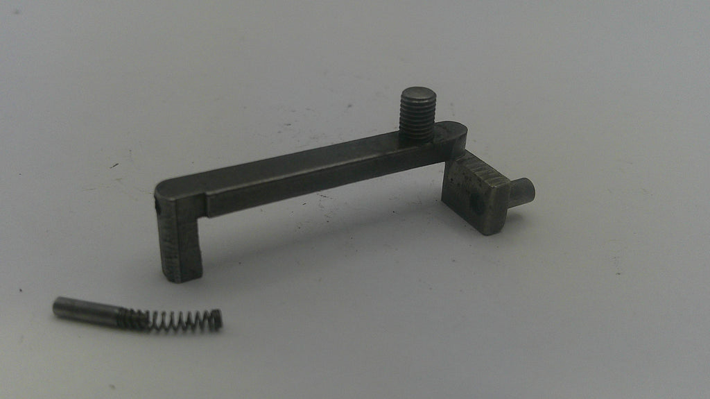 A small dark metal mechanical component with a threaded rod and a separate small spring, photographed on a plain light gray background.