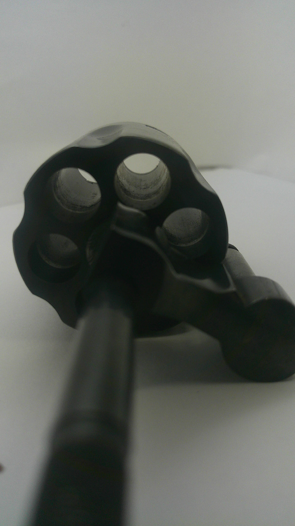 A close-up shot of a black revolver cylinder with a black barrel or tool inserted, set against a plain white background.