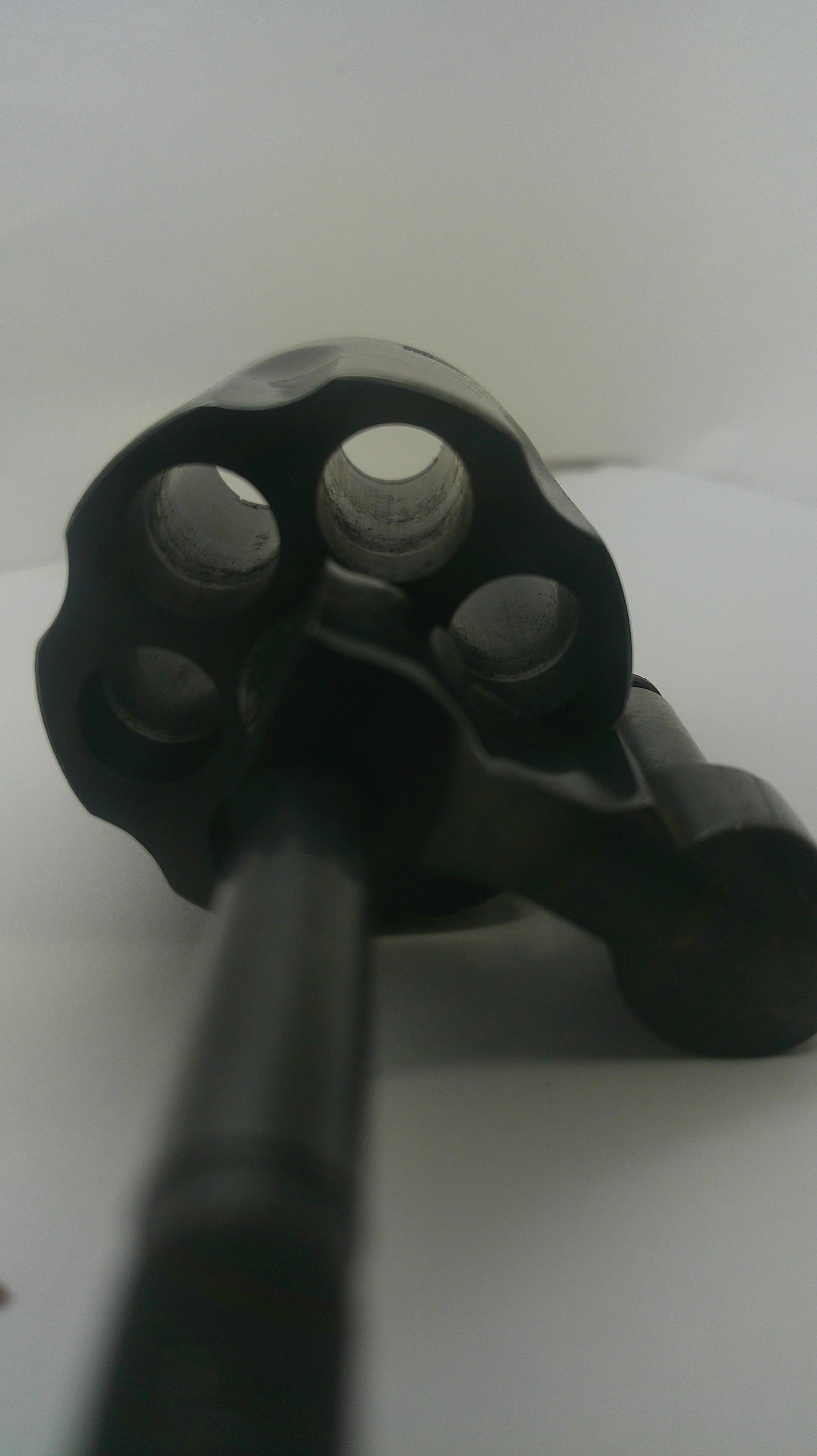 A close-up shot of a black revolver cylinder with a black barrel or tool inserted, set against a plain white background.