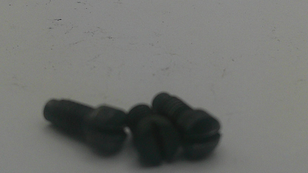 Three small black slotted flathead screws lying on a plain light gray surface.