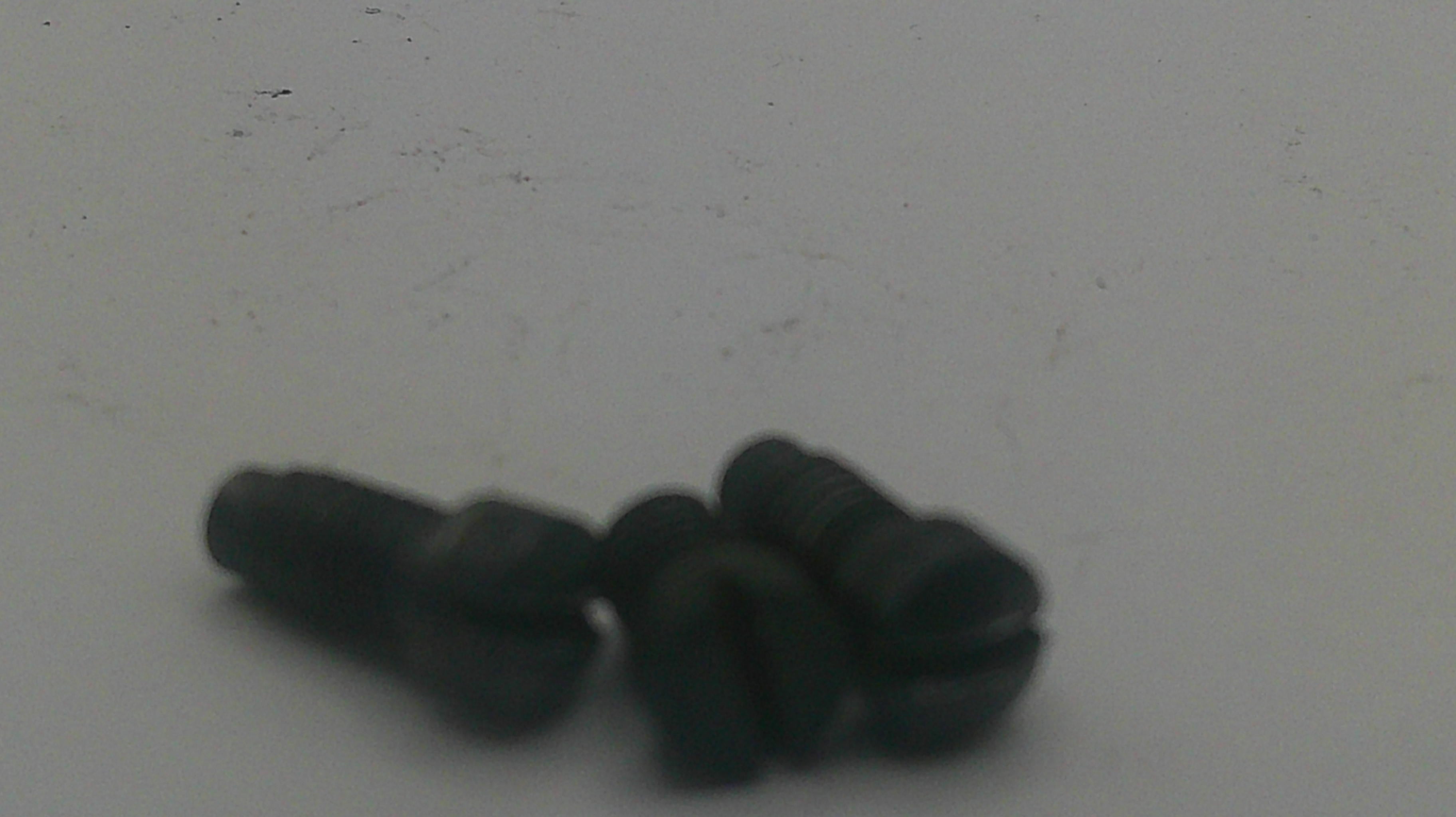 Three small black slotted flathead screws lying on a plain light gray surface.