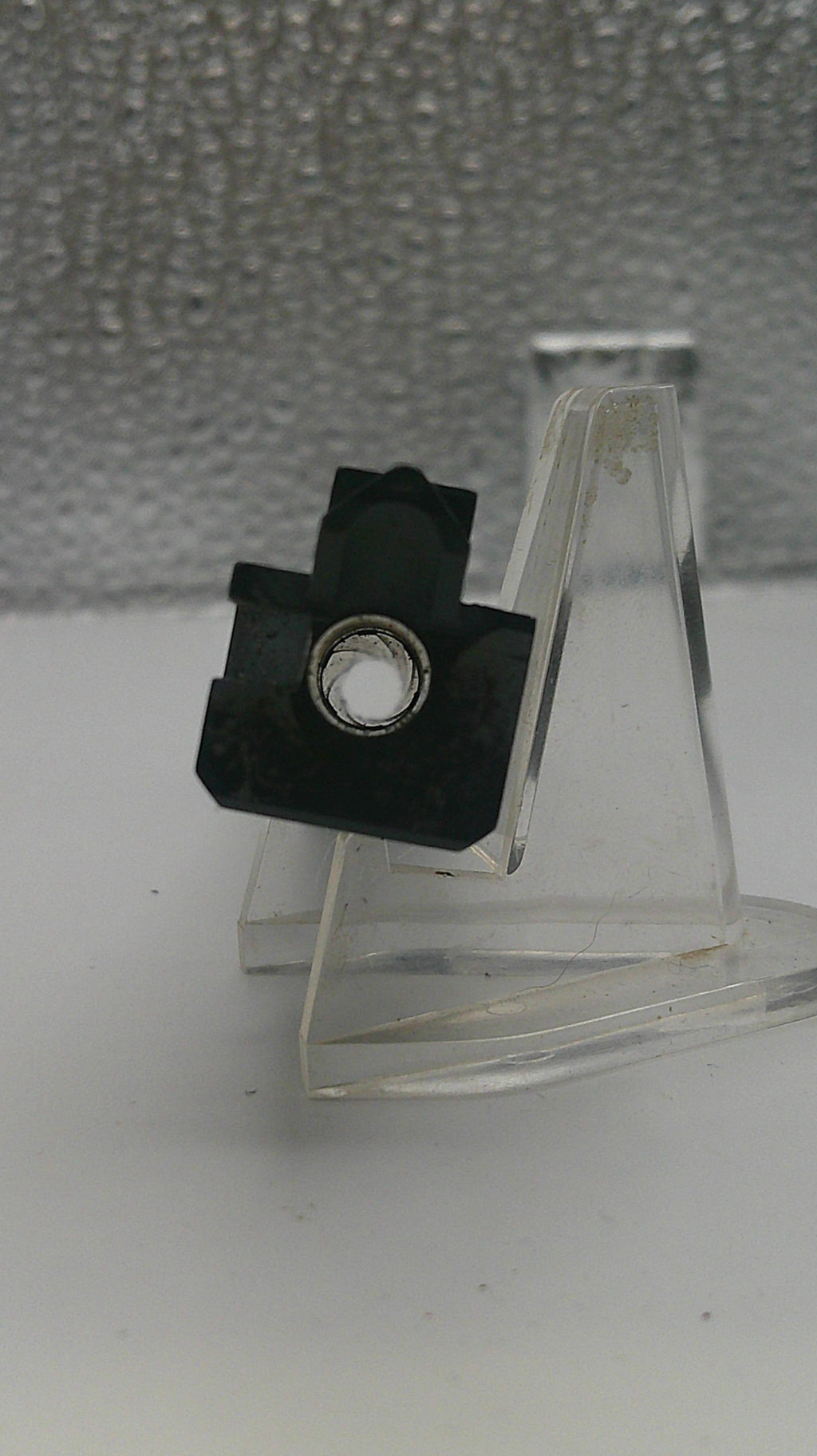 Clear plastic bracket with a black fastener on a textured gray background